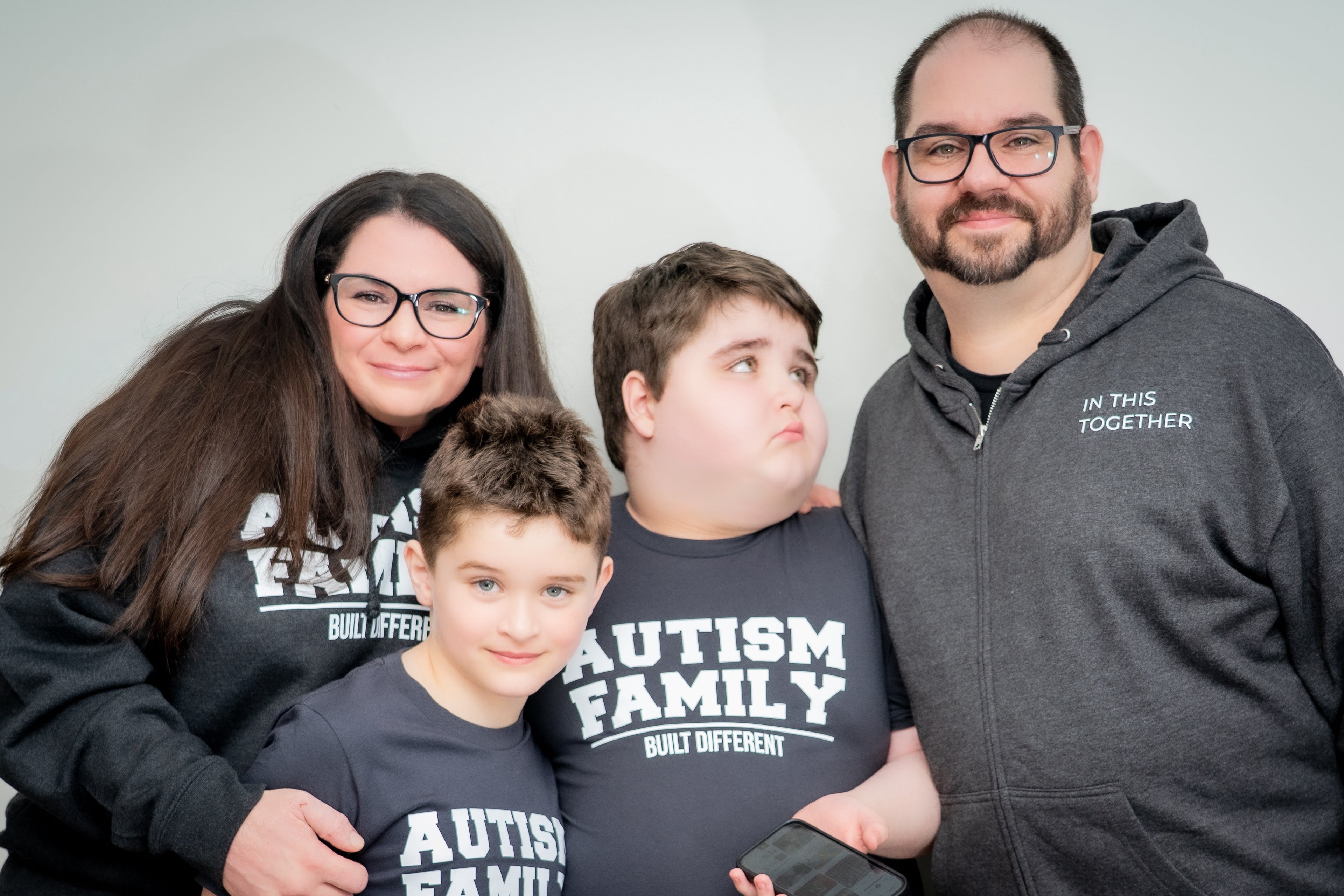 Family wearing shirts with 'Autism Family Built Different' text on a plain background